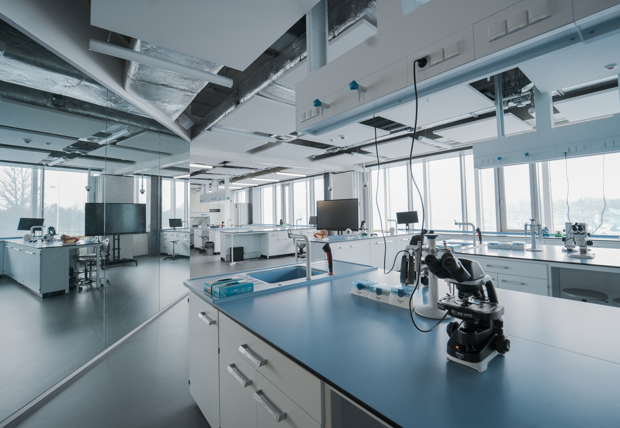 Zdjęcie przedstawia duże pomieszczenie z oknami, stanowiskami pracy, sprzętem (między innymi mikroskopami) i innymi urządzeniami do prowadzenia badań interdyscyplinarnych.