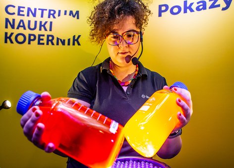 Animatorka na żółtym tle, w rękach trzyma kolorowe butelki