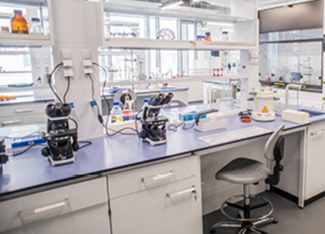 Na zdjęciu widać pomieszczenie z białymi stołami i szafkami oraz sprzętem badawczym