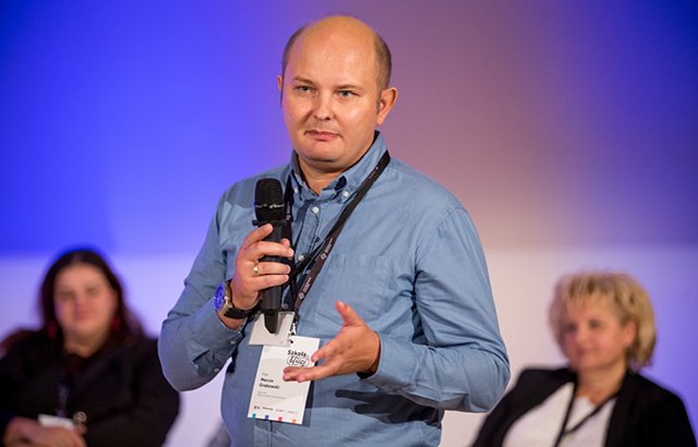 Na zdjęciu przemawiający w czasie spotkania dla uczestników projektu Marcin Grabowski. W rozmytym tle widać innych występujących w czasie tego spotkania.