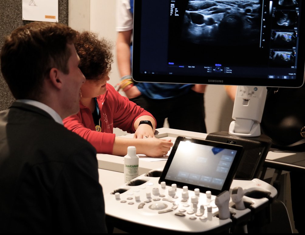 Dwoje ludzi, kobieta w czerwonej bluzie animatora i mężczyzna w garniturze przed ekranem do usg.