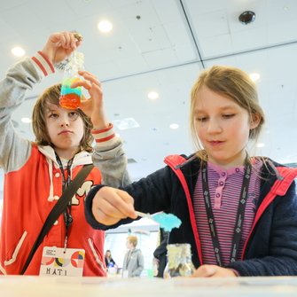 Dwoje dzieci przesypuje kolorowy proszek do butelek