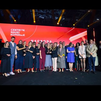  Zdjęcie grupowe laureatów i organizatorów gali Nagrody Przewroty na tle czerwonego ekranu z logo.