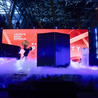  Scena z czerwonym ekranem Centrum Nauki Kopernik, efekty dymne i performerzy w trakcie pokazu.