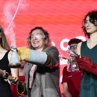  Trzy kobiety w goglach ochronnych prezentują dymiące kolby podczas pokazu naukowego.