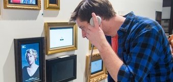 Człowiek wpatrujący się w ścianę pełną obrazków w ramkach.