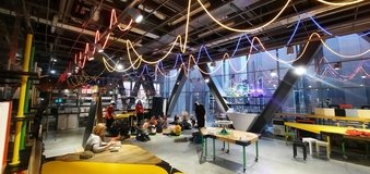 Widok przestrzeni warsztatowej z kolorowymi światłami pod sufitem, w dalekim planie widac grupę ludzi.