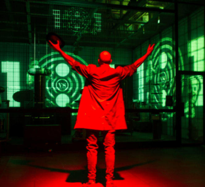 Ciemne pomieszczenie, na środku stoi tyłem podświetlona na czerwono osoba z uniesionymi rękami.