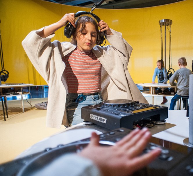 Nastolatka zakłada słuchawki na głowę, przed nią jest konsola muzyczna. 