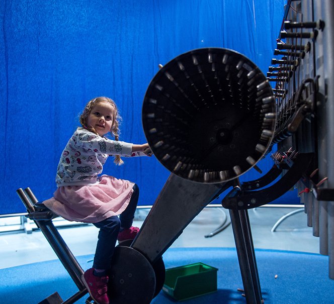 Dziewczynka siedząca przed wielkim bębnem jak wałki w katarynkach.