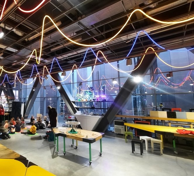 Widok przestrzeni warsztatowej z kolorowymi światłami pod sufitem, w dalekim planie widac grupę ludzi.