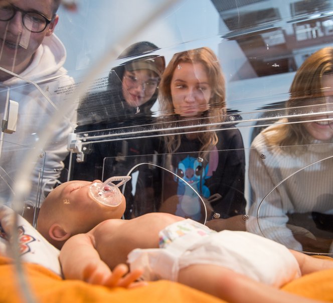 Ludzie pochyleni nad sztucznym niemowlakiem