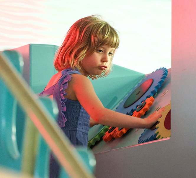 Dziewczynka bawi się kolorowymi kołami zębatymi na interaktywnej wystawie.