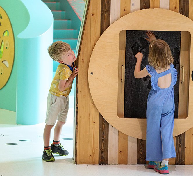 Dzieci przy instalacji z czarną tablicą, jedna z nich zostawia odcisk dłoni.