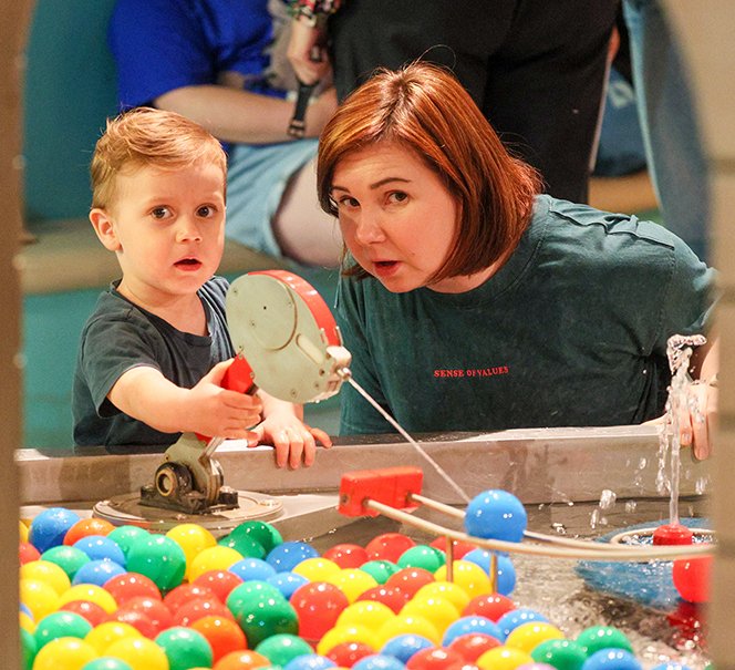 Chłopiec i kobieta przyglądają się instalacji wodnej z kolorowymi piłeczkami.