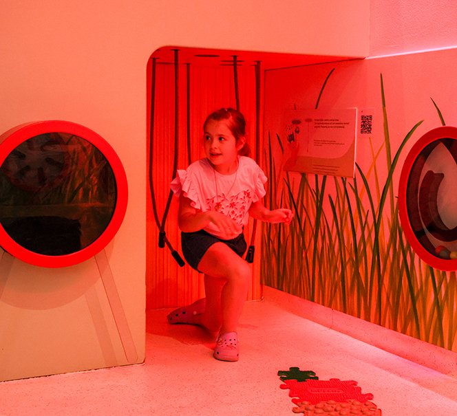 Dziewczynka wychodzi z czerwonej przestrzeni edukacyjnej, patrząc w bok.