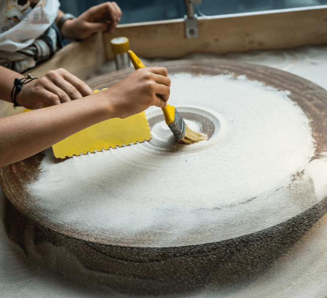 Dziecięce dłonie przesypują piasek i używają pędzla do odkrywania wzorów na obracającym się kole.